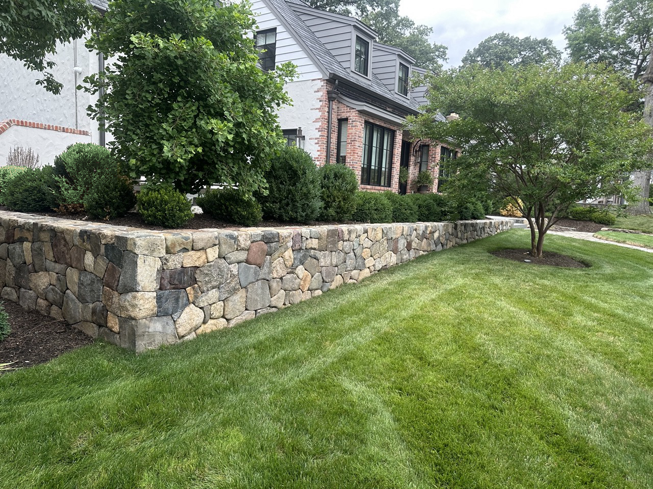 Long fieldstone retaining wall with boxwood and ornamental trees