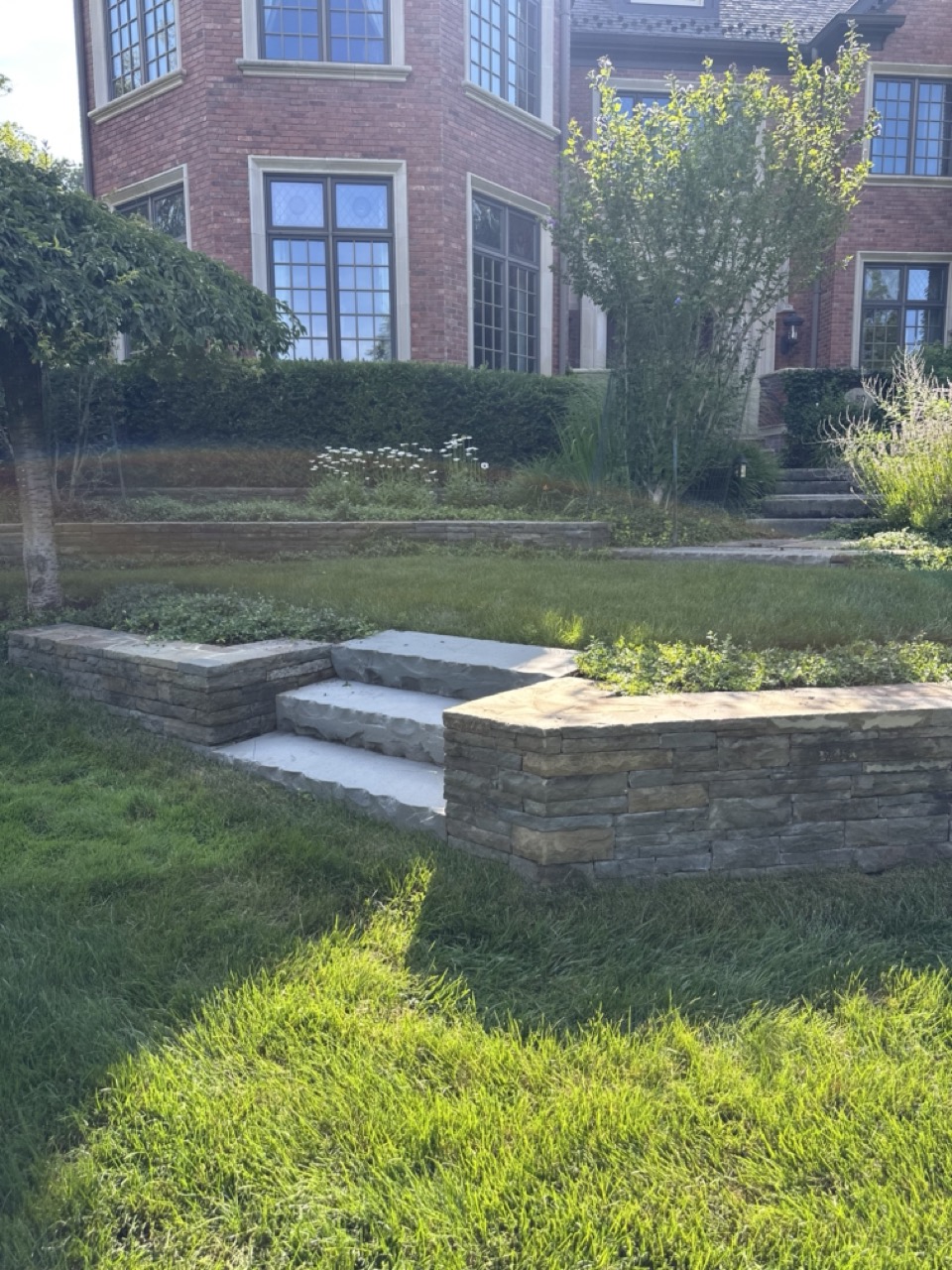 Stone retaining walls with bluestone steps and manicured lawn approaching the Tudor estate